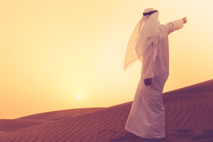 An Arab standing at the sand dunes of Dubai and aiming towards the horizon.