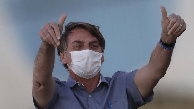 FILE - In this  July 17, 2020, file photo, Brazil's President Jair Bolsonaro who is infected with COVID-19, wears a protective face mask as he flashes thumbs-up at supporters during a Brazilian flag retreat ceremony outside his official residence Alvorada Palace, in Brasilia, Brazil. Bolsonaro announced his illness in July and used it to publicly extol hydroxychloroquine, the unproven malaria drug that he’d been promoting as a treatment for COVID-19 and was taking himself. (AP Photo/Eraldo Peres, File)