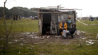 Sebuah keluarga duduk di depan rumah kecil yang terbuat dari lembaran seng di Guernica, provinsi Buenos Aires, Argentina.