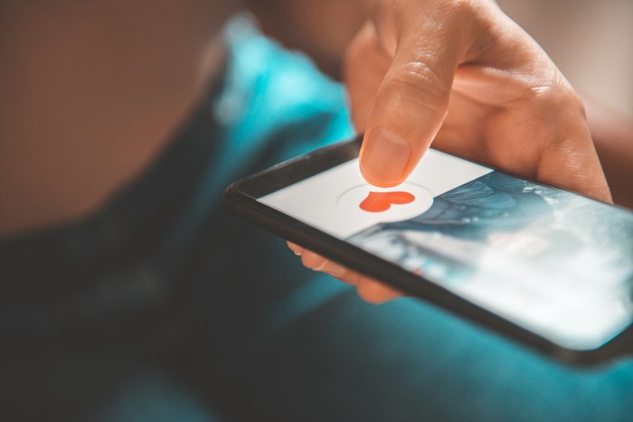 Finger of woman pushing heart icon on screen in mobile smartphone application. Online dating app, valentines day concept.