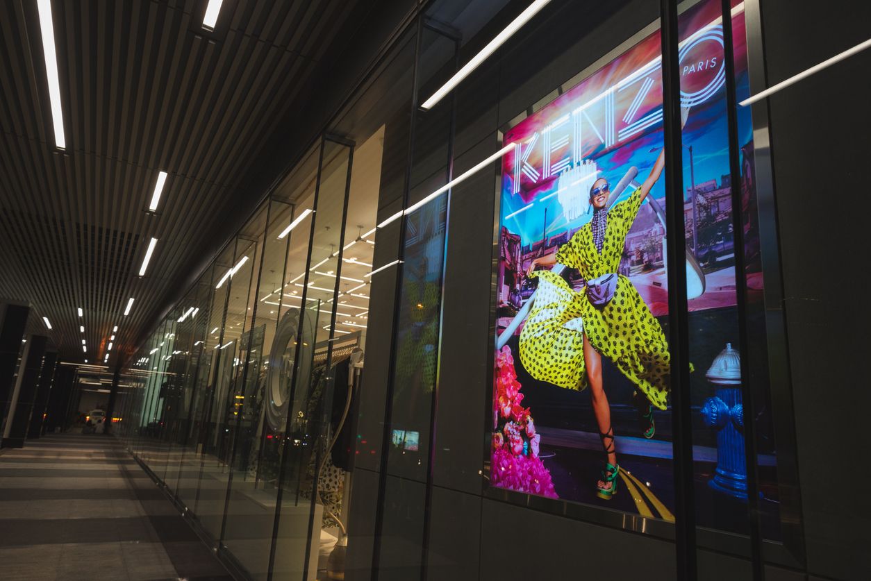 Kenzo Takada Ho Chi Minh City, Vietnam - April 23, 2019: a Kenzo shop exterior at a night colonnade of Saigon Centre Shopping Mall, with a colorful promotional poster. A taxi car (blurred) seen in the end of the colonnade.