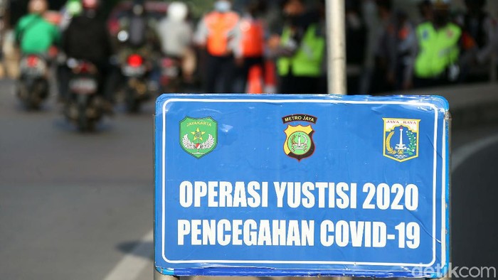 Polisi melakukan Operasi Yustisi untuk penegakan penerapan protokol kesehatan. Polisi bersenjata laras panjang terlihat berjaga dalam operasi tersebut.