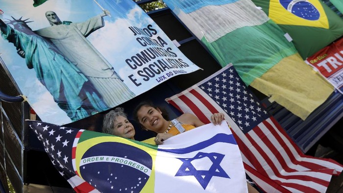 Demonstrators take photos in front of flags and a sign with the Statue of Liberty is embraced by Christ the Redeemer and the written in Portuguese that reads 
