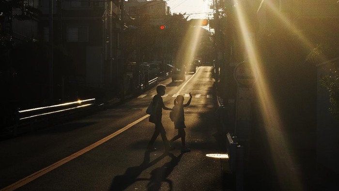 A child and her guardian walk across the street as they were silhouetted in the late afternoon sunlight Monday, Oct. 5, 2020, in Yokohama,Japan. (AP Photo/Kiichiro Sato)