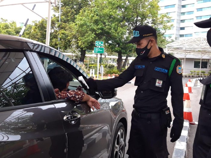 Petugas keamanan DPR mengecek suhu tubuh pengendara mobil dengan thermo gun sebelum memasuki kompleks parlemen