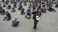 Seorang orator menyuarakan orasinya di depan para massa aksi yang duduk di lingkaran social distancing. 