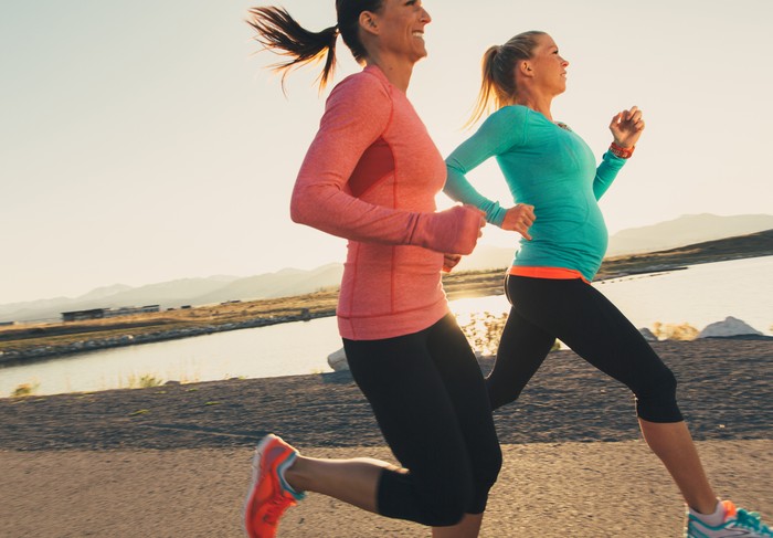 olahraga ibu hamil Two female runners in pink and blue athletic shirts are training for their next race. These women enjoy running at sunset in the evening together as friends on the trails through. Running is their way of staying active and healthy.