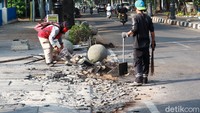 Petugas membersihkan puing-puing pot yang pecah di atas trotoar.