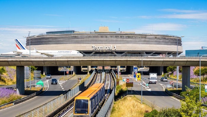 Roissy-en-France, France - July 27, 2020: View on the Terminal 1 of Paris-Charles de Gaulle Airport with an Air France airliner rolling on a taxiway bridge above the roads and airport shuttle line.