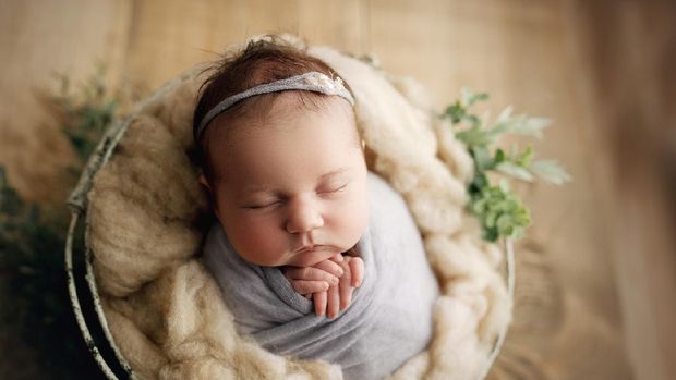 20 day old baby girl with chunky cheeks, swaddled in pale purple with a matching headband, in a prop basket for her newborn milestone photos