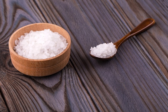 White bath salt in a wooden bowl with a spoon on a wooden table