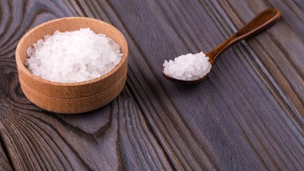 White bath salt in a wooden bowl with a spoon on a wooden table