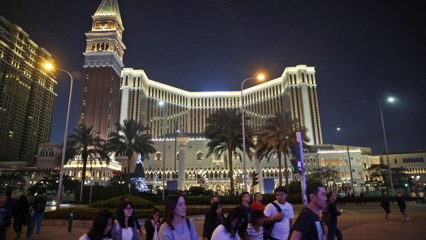 FILE - In this Nov. 23, 2014, file photo, people walk across a road in front of the Venetian Macao casino resorts in Macau. An earnings report suggested Wednesday, April 17, 2019, that Las Vegas Sands Corp. paid $96 million to settle a 15-year breach-of-contract dispute with Richard Suen, a Hong Kong businessman who helped the U.S. company open its first casino in the Chinese gambling enclave of Macau. (AP Photo/Kin Cheung, File)