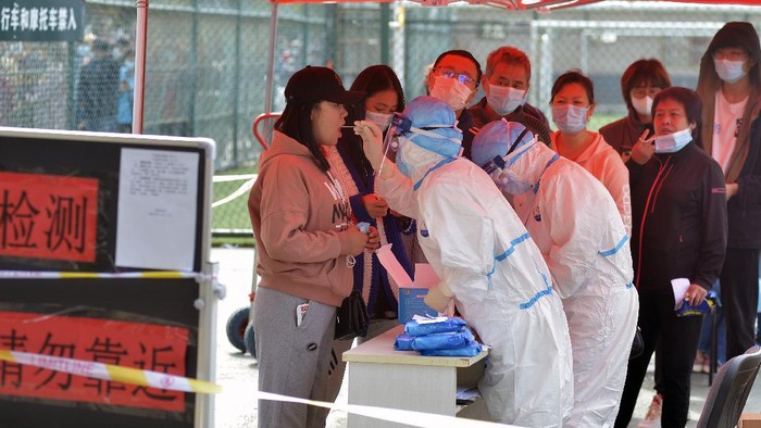 A medical staff takes a swab from a woman as residents line up for the COVID-19 test near the residential area in Qingdao in east Chinas Shandong province, Monday, Oct. 12, 2020. Chinas government says all 9 million people in the eastern city of Qingdao will be tested for the coronavirus this week after nine cases linked to a hospital were found. The announcement Monday broke a string of weeks without any locally transmitted infections reported in China. (Chinatopix via AP)