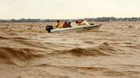 Dengan menggunakan perahu motor, tim penyelamat melintasi derasnya aliran sungai menuju permukiman yang terendam banjir. Otoritas manajemen kebencanaan Vietnam mengatakan, lebih dari 130.000 rumah terkena dampak. Nguyen Van Ty/VNA via AP.
