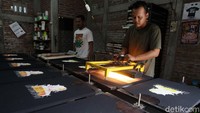 Pekerja mengeringkan kaos saat penyablonan dengan bantuan lampu dan hairdryer.