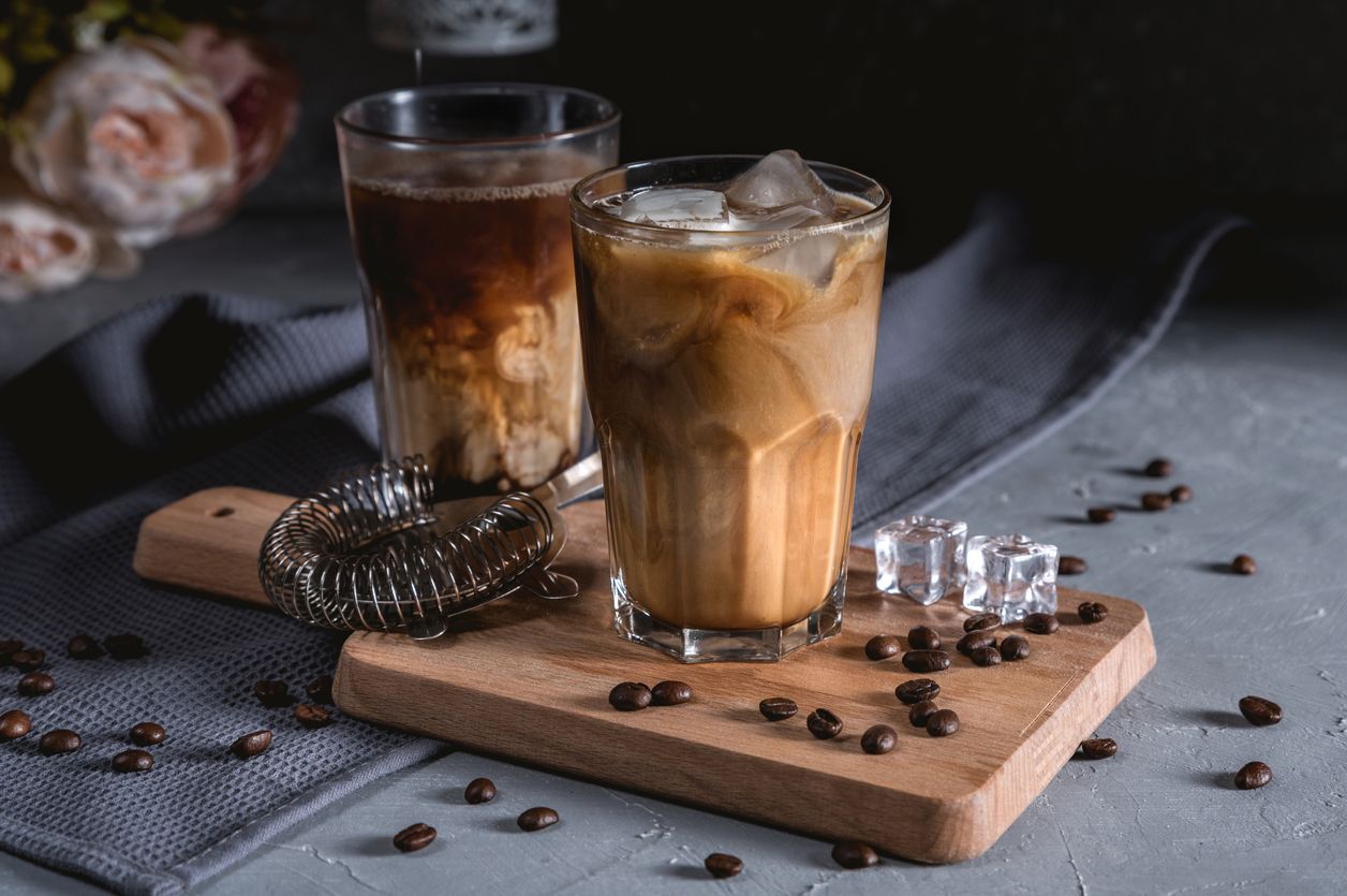 Iced coffee in a tall glass with cream on dark background