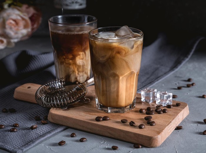 Iced coffee in a tall glass with cream on dark background