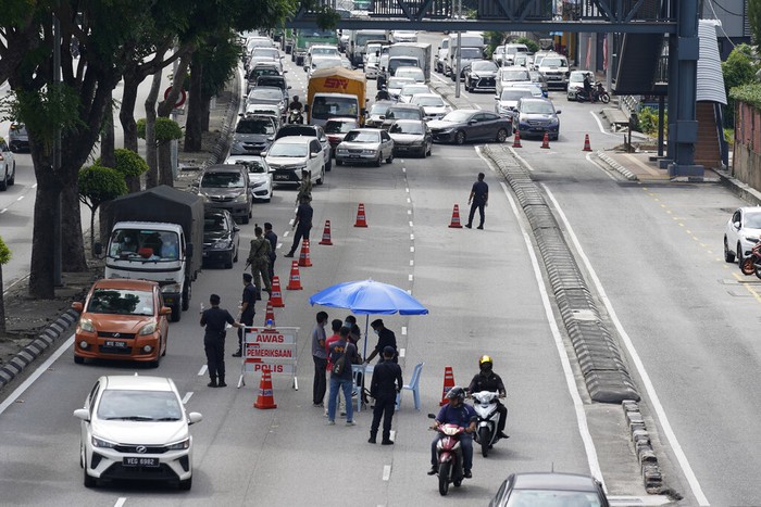 Police officers check vehicles at a roadblock to ensure that people abide by a movement control order on the outskirts of Kuala Lumpur, Malaysia, Wednesday, Oct. 14, 2020. Malaysia will restrict movements in its biggest city Kuala Lumpur, neighboring Selangor state and the administrative capital of Putrajaya from Wednesday to curb a sharp rise in coronavirus cases. (AP Photo/Vincent Thian)