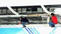 Dua orang pekerja sedang memperbaiki plafon halte yang rusak.