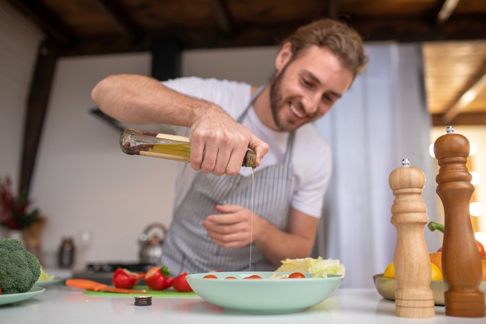 Pria memasak dengan minyak zaitun Filling a salad. A concentrated cook putting some oil into a salad
