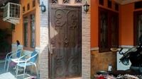Halaman rumah tak terlihat luas, hanya diisi dua bangku besi beserta satu meja. Terlihat ada beberapa tanaman di depannya. Begitu masuk ke dalam rumah terlihat ruang tamu dengan 3 kursi kayu berwarna hijau dan satu meja.