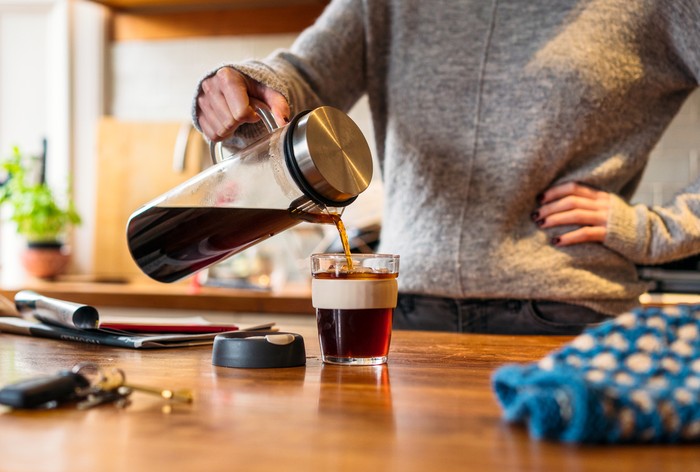 A woman pouring cold-brew coffee into a re-usable mug in the kitchen.