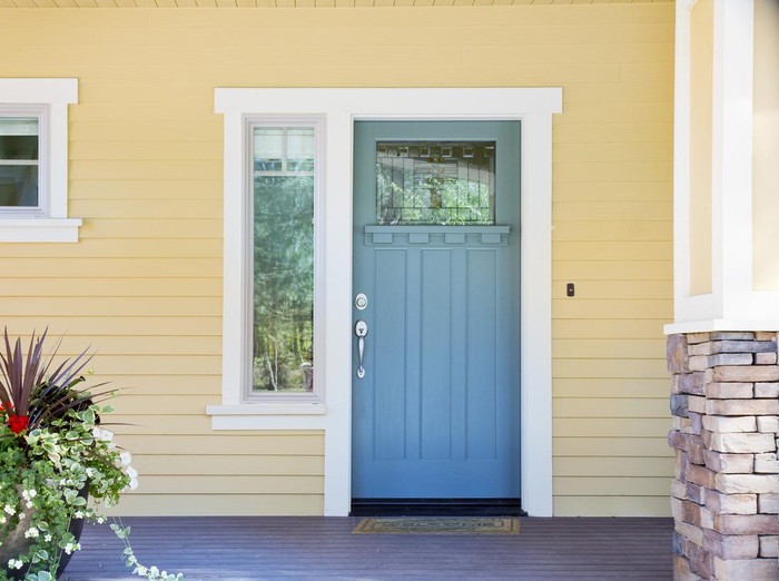 Panorama frame The red front door of a house with concrete exterior wall and shutters on window. Doormat and potted flowers are placed by the doorstep.