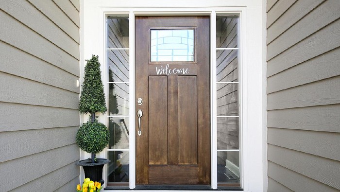 Panorama frame The red front door of a house with concrete exterior wall and shutters on window. Doormat and potted flowers are placed by the doorstep.