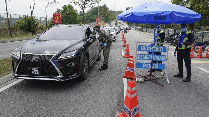 Police officers check vehicles at roadblock to ensure that people abide by the movement control order on the outskirts of Kuala Lumpur, Malaysia, Wednesday, Oct. 14, 2020. Malaysia will restrict movements in its biggest city Kuala Lumpur, neighboring Selangor state and the administrative capital of Putrajaya from Wednesday to curb a sharp rise in coronavirus cases. (AP Photo/Vincent Thian)