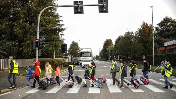 Children, escorted by volunteers, walk to school holding on to a rope to help maintain social distancing and curb the spread of COVID-19, in Bellusco, northern Italy, Tuesday, Oct. 20, 2020. (AP Photo/Luca Bruno)