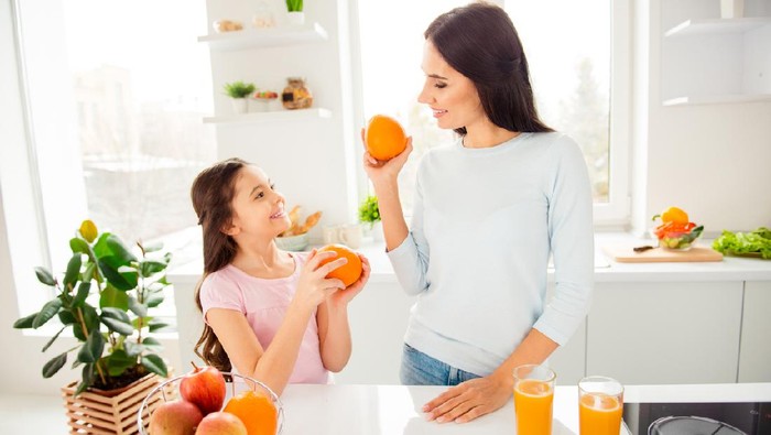 Beautiful lovely nice charming cheerful mom and her small little daughter in casual, holding, showing each other grapefruits, healthy natural orange fresh juice on table in light kitchen