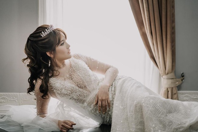 Untuk momen spesial tersebut, perempuan 33 tahun ini menebar pesonanya dalam balutan gaun putih berhiaskan embellishment yang berkilauan. Neckline gaun yang rendah sukses mengakomodasi keseksian Angela. (Foto: Instagram/@memoirastudio)