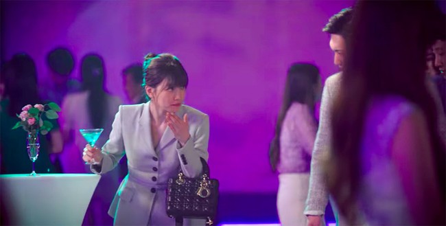 Bae Suzy mengenakan setelan blazer bernuansa nude saat beradegan di sebuah pesta kantor. Ia pun tampak mengenakan tas Lady Dior yang ikonik. Foto: Dok. Start-Up/Netflix