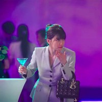 Bae Suzy mengenakan setelan blazer bernuansa nude saat beradegan di sebuah pesta kantor. Ia pun tampak mengenakan tas Lady Dior yang ikonik. Foto: Dok. Start-Up/Netflix