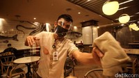 Seorang petugas sedang membersihkan sekat plastik yang terpasang di meja makan area restoran tersebut.