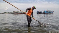 Petugas membersihkan sampah yang mengambang di saat banjir.