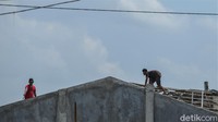 Dua orang warga tampak sedang memperbaiki bagian atap rumahnya yang rusak dihantam angin puting beliung.