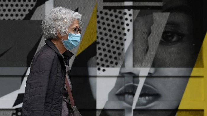A woman wearing a face mask walks past a graffiti in Barcelona on October 21, 2020. - Spain has become one of the pandemics hotspots in the European Union, with close to 975,000 registered cases and nearly 34,000 deaths. (Photo by LLUIS GENE / AFP)