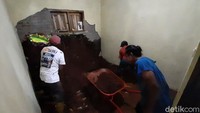 Warga membersihkan material longsor yang menerjang sebuah rumah.