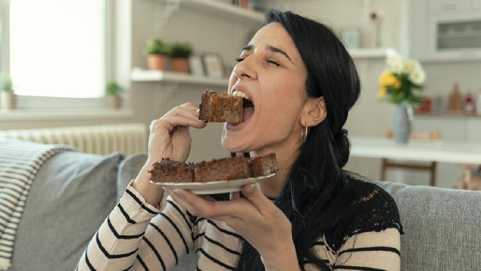Young Woman Eating Unhealthy Food. Sweetness Indulging and Fattening Concept. Girl Biting Chocolate Cake, High-calorie Sweet Food, Increased Glucose Diabetes. Sweet food addiction.