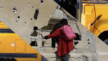 Seorang siswi Suriah melintasi tembok yang rusak di luar sekolahnya di kota Kobane, Suriah, juga dikenal sebagai Ain al-Arab, pada 25 Maret 2015. Foto: Uğur Gallenkuş