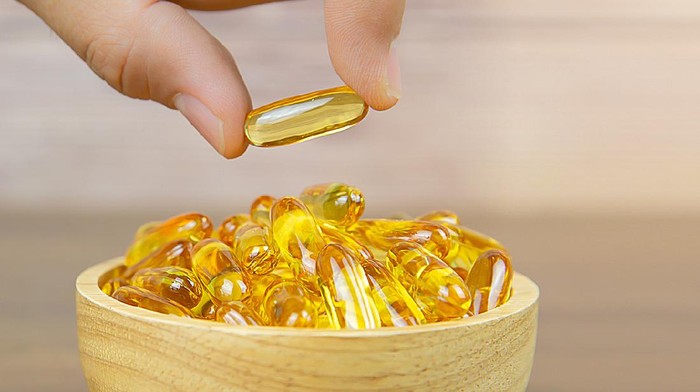 Hand picked cod liver oil capsule or fish oil in a wooden cup. Dietary supplement for health-care concepts.