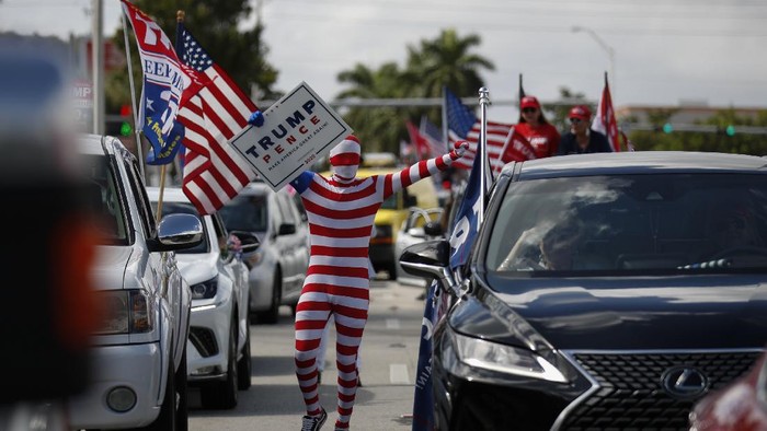 A man wearing a flag-themed body stocking walks between lines of cars as hundreds of vehicles gather for a car caravan in support of President Donald Trump, at Tropical Park in Miami, Sunday, Nov. 1, 2020. (AP Photo/Rebecca Blackwell)