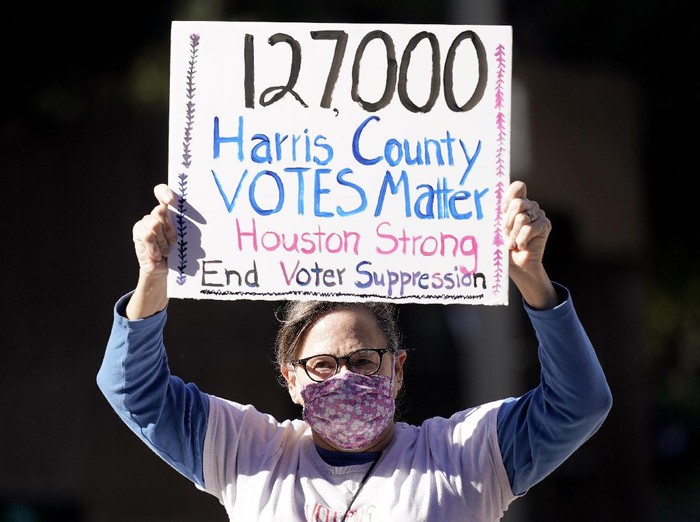 Demonstrator Gina Dusterhoft holds up a sign as she walks to join others standing across the street from the federal courthouse in Houston, Monday, Nov. 2, 2020, before a hearing in federal court involving drive-thru ballots cast in Harris County. The lawsuit was brought by conservative Texas activists, who have railed against expanded voting access in Harris County, in an effort to invalidate nearly 127,000 votes in Houston because the ballots were cast at drive-thru polling centers established during the pandemic. (AP Photo/David J. Phillip)