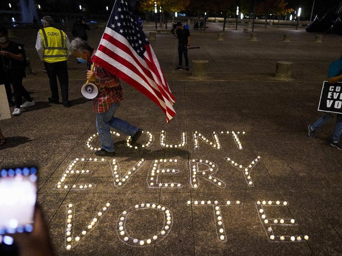 Benny De La Vega carries the American flag as he places candles on the words 