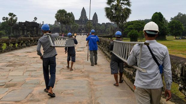 This photo taken on October 12, 2020 shows a gardener throwing down tree saplings removed from the exterior of the Angkor Wat temple in Siem Reap province. - Stacking a ladder against the towering spires of Cambodia's archaeological marvel Angkor Wat, a crack team of gardeners gingerly scales the temple's exterior to hack away foliage before it damages the ancient facade. (Photo by TANG CHHIN Sothy / AFP) / TO GO WITH Cambodia-archaeology-culture-conservation, FEATURE by Suy SE