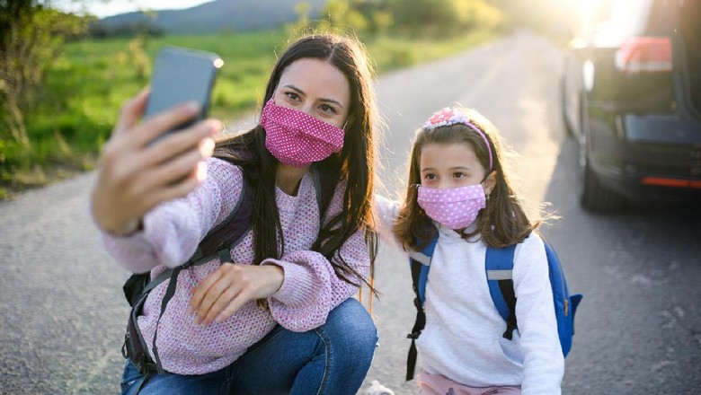 Liburan saat Corona Mother with small daughter taking selfie with smartphone on trip outdoors in nature, wearing face masks.