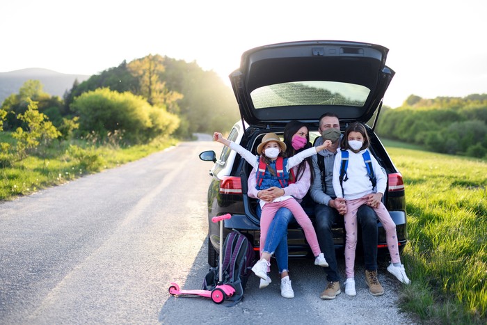 Front view of family with two small daughters on trip outdoors in nature, wearing face masks.