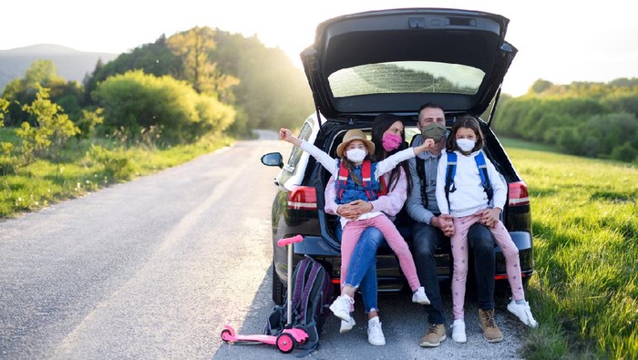 Front view of family with two small daughters on trip outdoors in nature, wearing face masks.